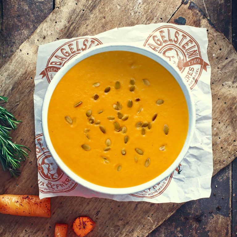 Un bol de soupe aux carottes sur une planche à découper en bois.